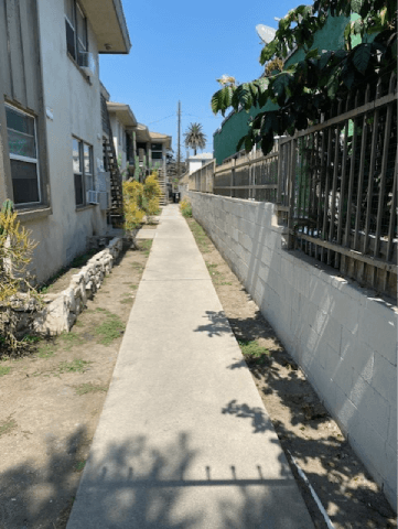 A concrete pathway leads down a street between two houses.