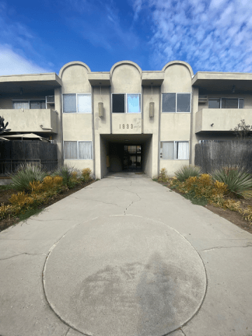 A concrete walkway leads to a building with a circular design on the ground.