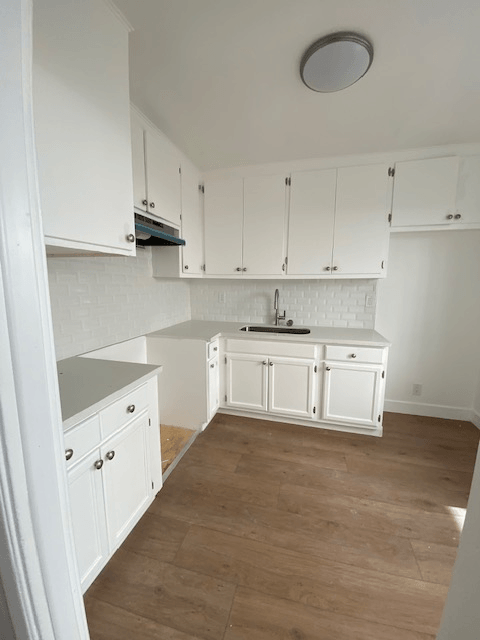 A kitchen with white cabinets and a white backsplash.