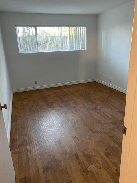 A room with wooden flooring and a window with blinds.