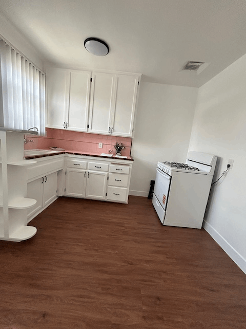 A kitchen with white cabinets and a pink backsplash.