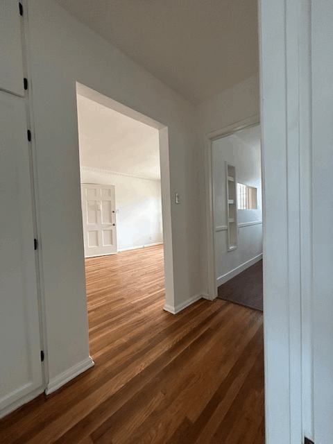 A hallway with a wooden floor and white walls.