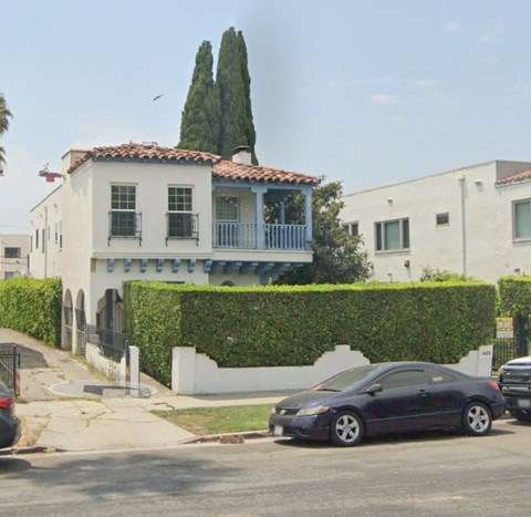A black car is parked in front of a white house with a red tile roof.