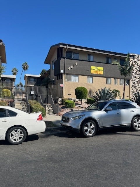 A silver car is parked in front of a building with a sign that reads "NO PARKING ANYTIME.".