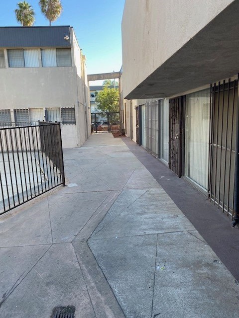 A long concrete walkway between two buildings with a black fence on the left.