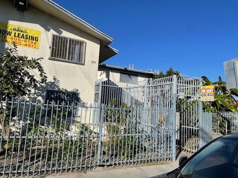 A car is parked in front of a fence with a sign that says "Now Leasing".