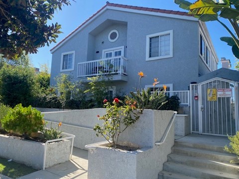 A house with a grey exterior and a red roof with a white fence and a gate.