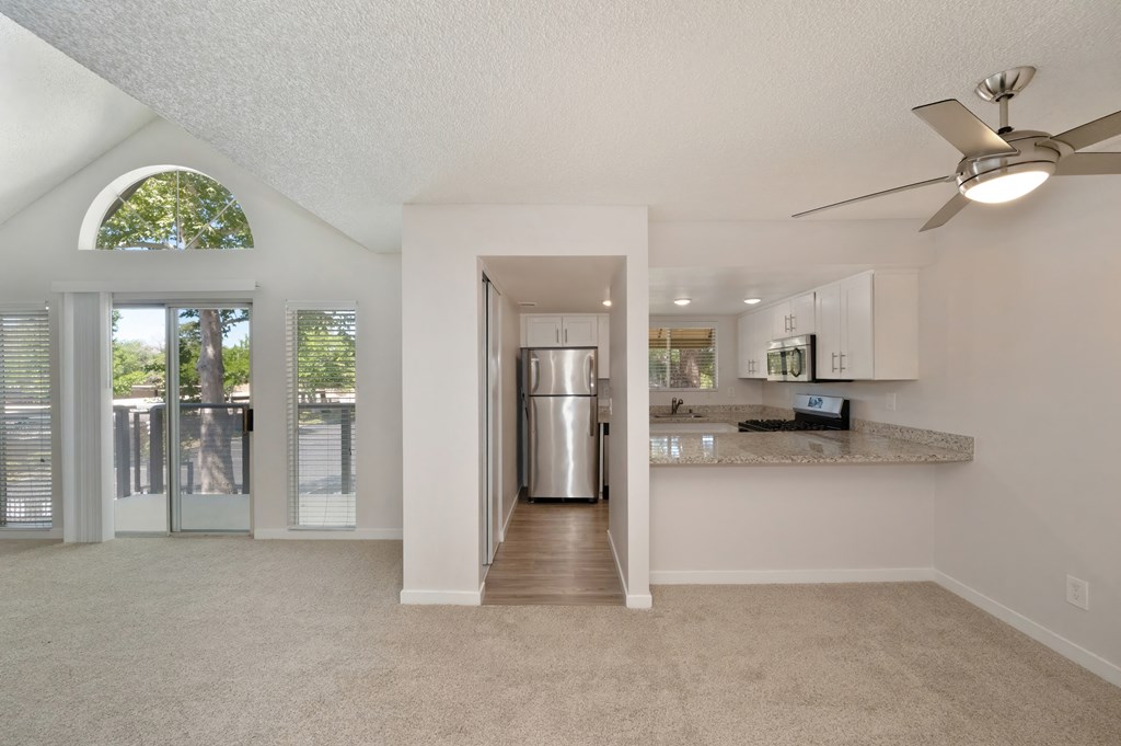 a living room with a view of a kitchen and a door to a balcony