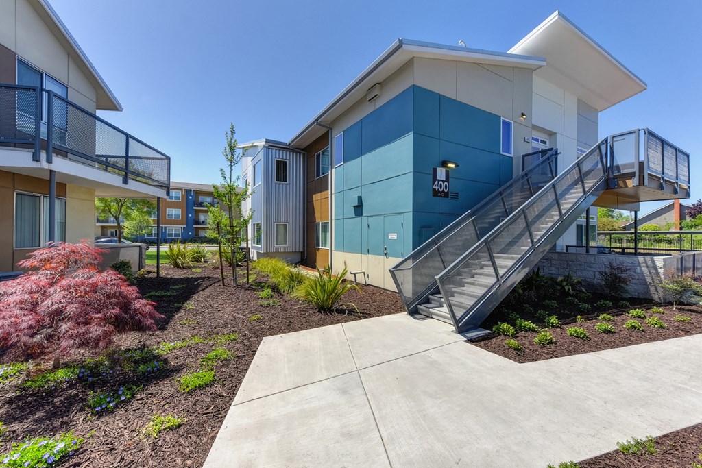 Apartment Exterior with Walking Path, Lavender Tree, Wood Chip Floor, Blue Apartment Exterior with Staircase at Addison Ranch Apartments, California