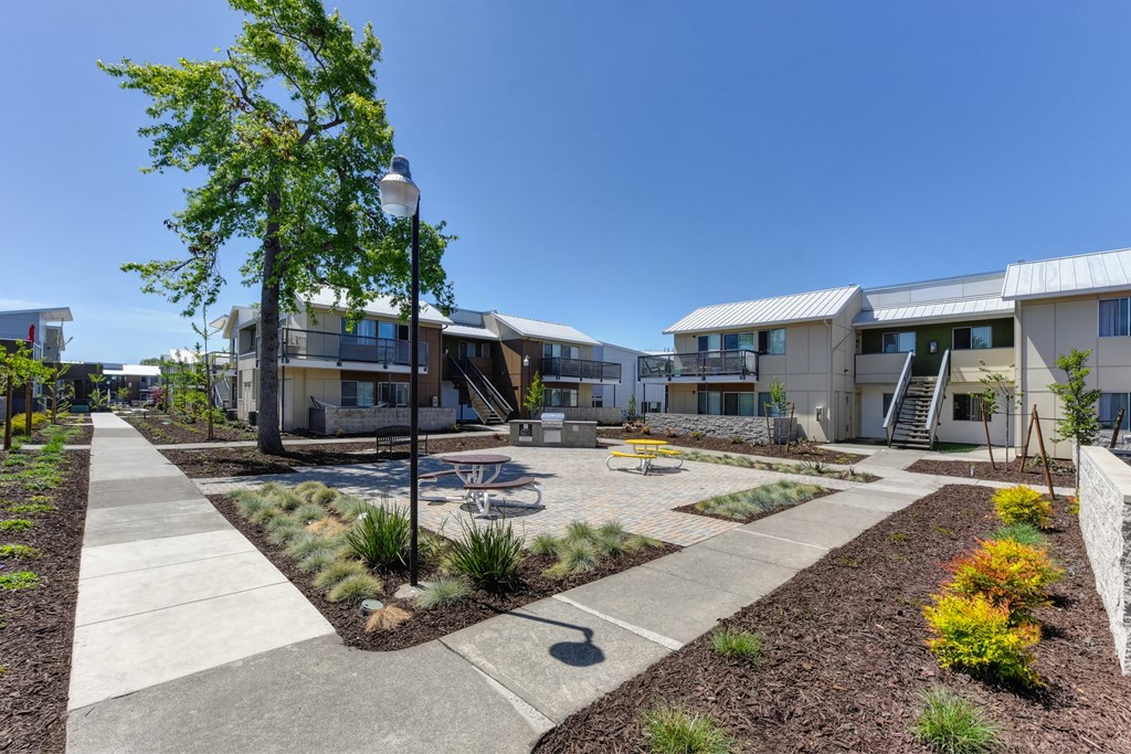 Outdoor Lounge Space with Red Picnic Table, Trees, Wood Chip Floor, Apartment Exterior at Addison Ranch Apartments, Petaluma, 94954