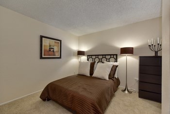 Furnished Bedroom with queen size bed, tall dresser and two floor lamps. Room is carpeted and with beige paint. - Photo Gallery 5