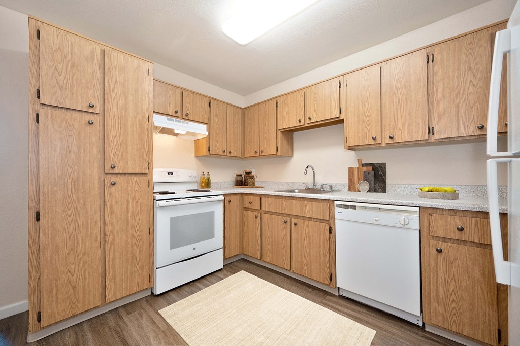 a kitchen with white appliances, wooden cabinets & hardwood inspired flooring 