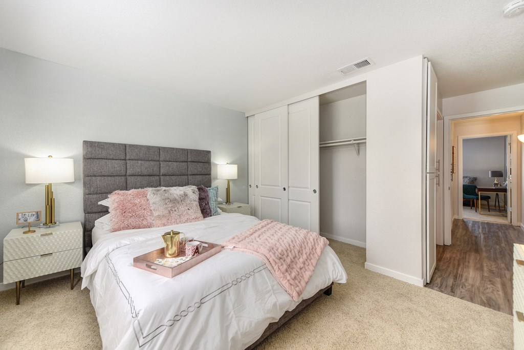Bedroom with Hallway, Carpet, White Bedside Dresser with Lamp and Open Closet at The Legacy Apartments, Antelope, California