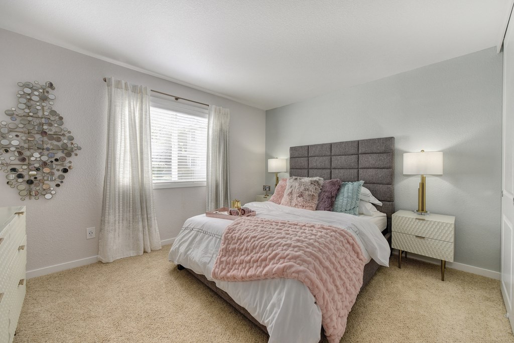 Bedroom with Carpet, Gray Head Board, White Bedside Dresser and Lamp at The Legacy Apartments, Antelope, CA