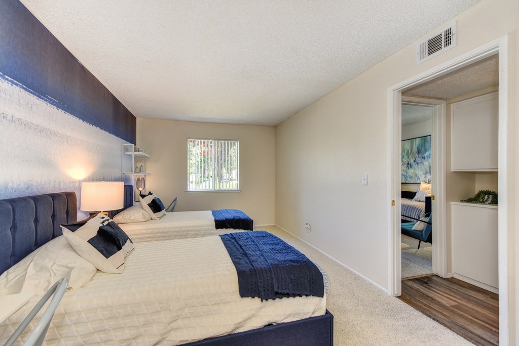 Bedroom with 2 twin beds with blue and white bedding.  Washer and dryer visible in hallway at Renaissance Park Apartments, Davis, California