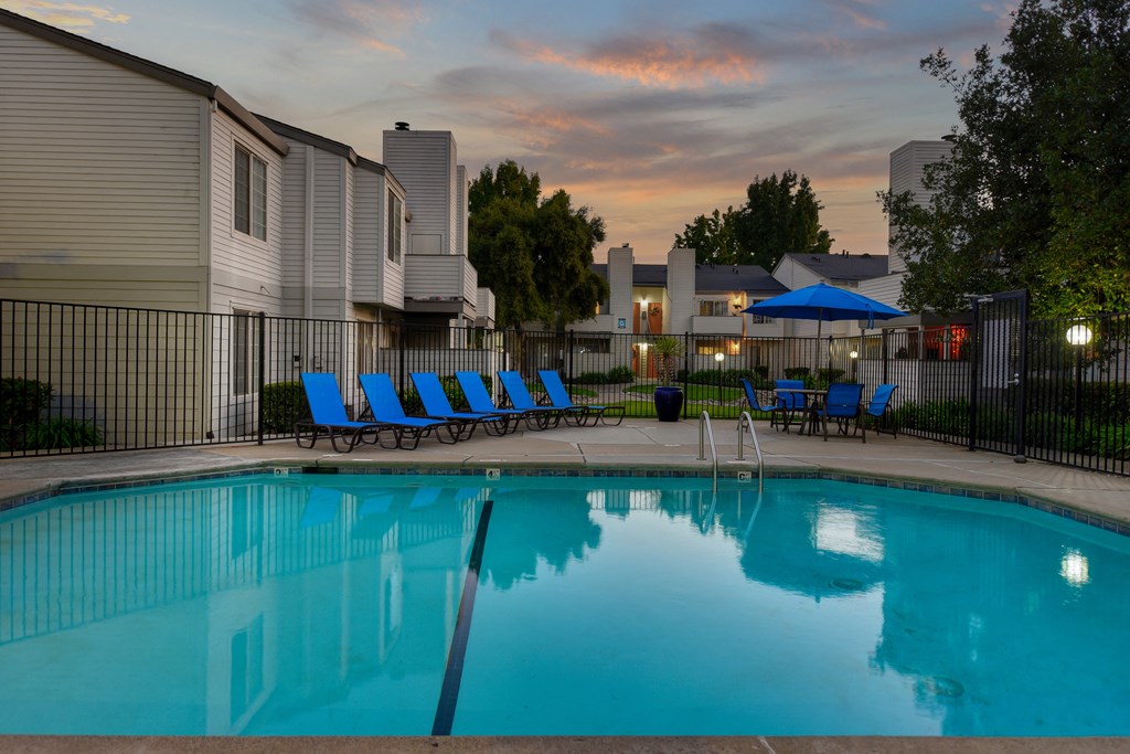 Swimming Pool Lounge Area at dusk with bright blue chairs and umbrellas at Cobblestone Creek Apartments, Roseville