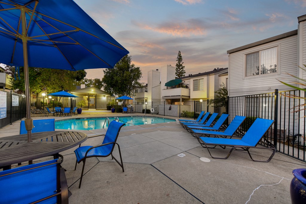 Swimming Pool Lounge Area at dusk with bright blue chairs and umbrellas at Cobblestone Creek Apartments, Roseville