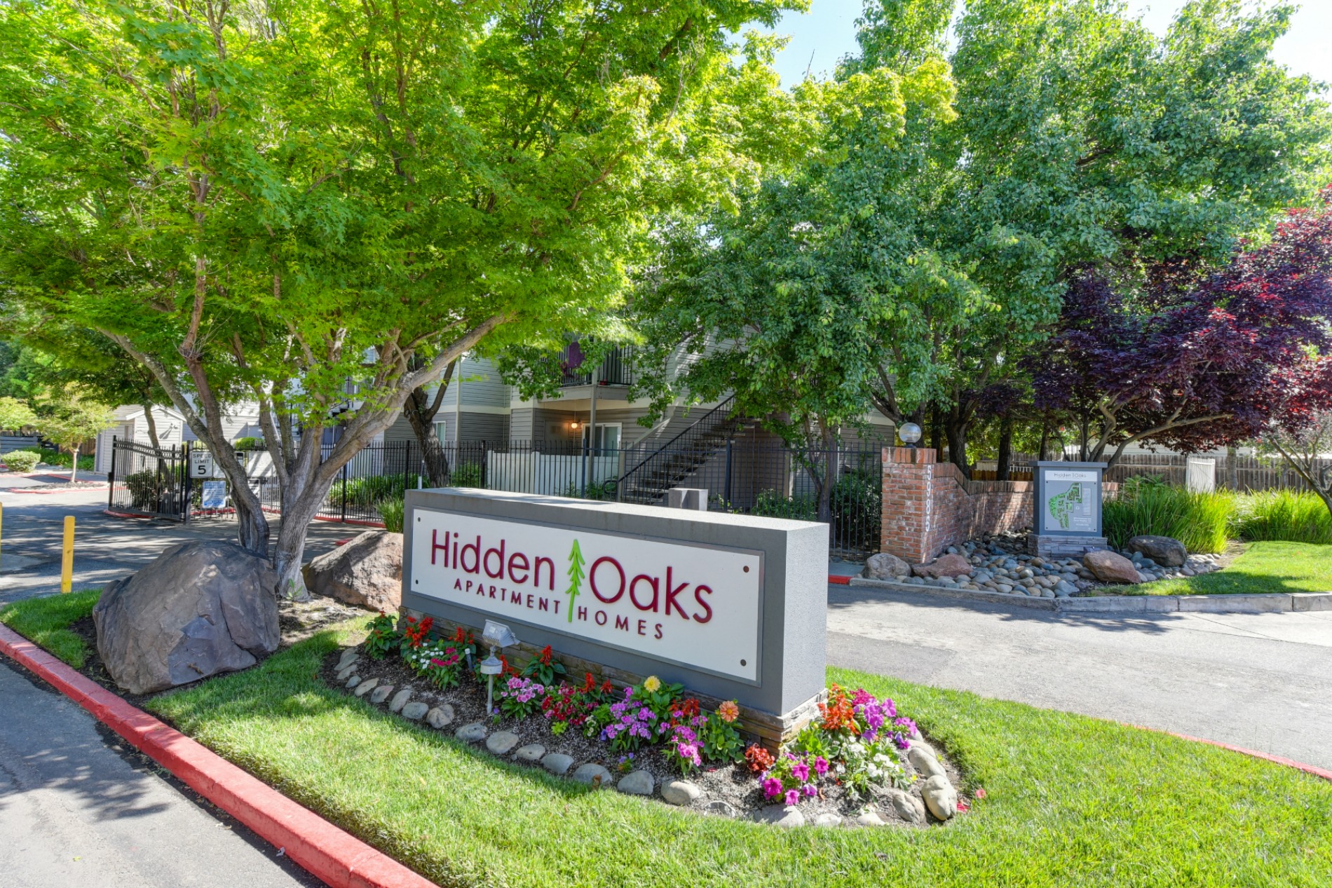 Community Entrance with Sign, Grass, Flower Bed, Trees and Road at Hidden Oaks Apartments, California, 95621