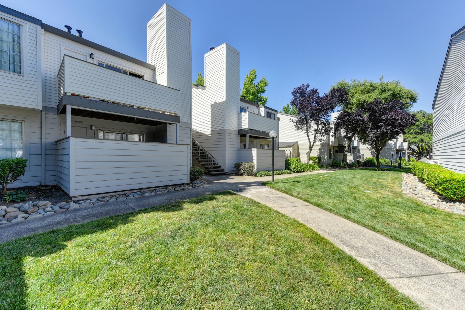 Walking Path with green grass and exterior of buildings in the distance at Cobblestone Creek Apartments, Roseville, CA