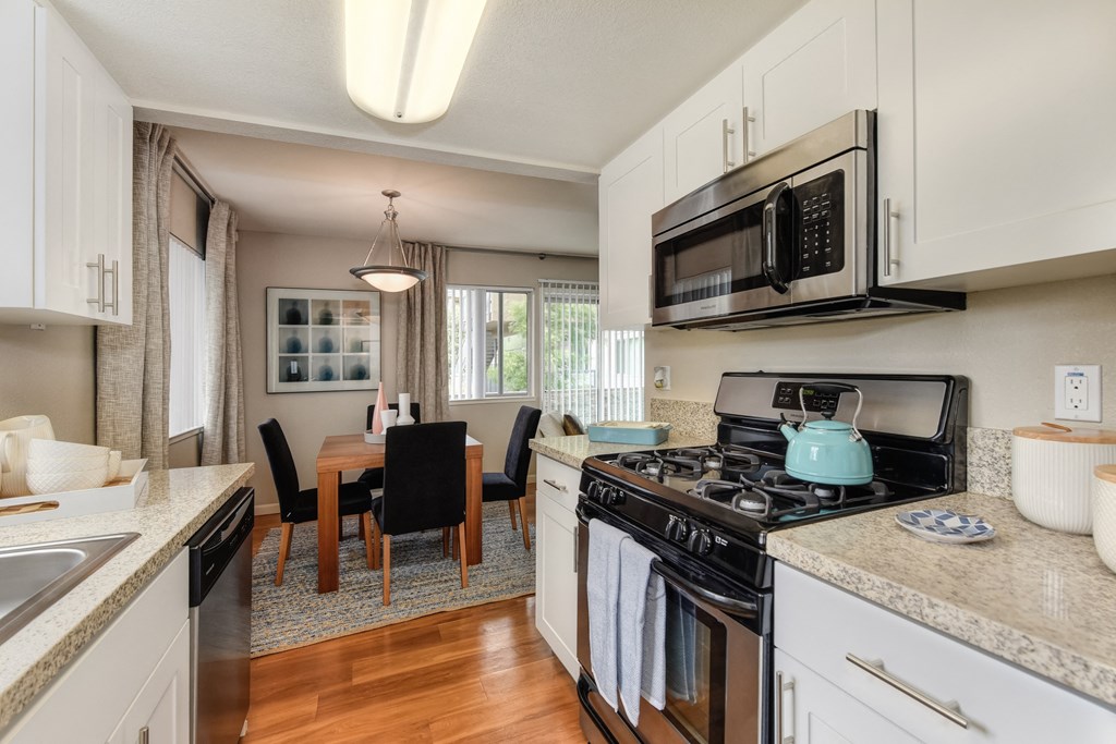 Dining Room/Kitchen with Wood Inspired Floor, Rug, Oven, Stove with Blue Tea Kettle, Microwave, Wood Dining Room Table and Chairs at Addison Ranch Apartments, Petaluma, 94954