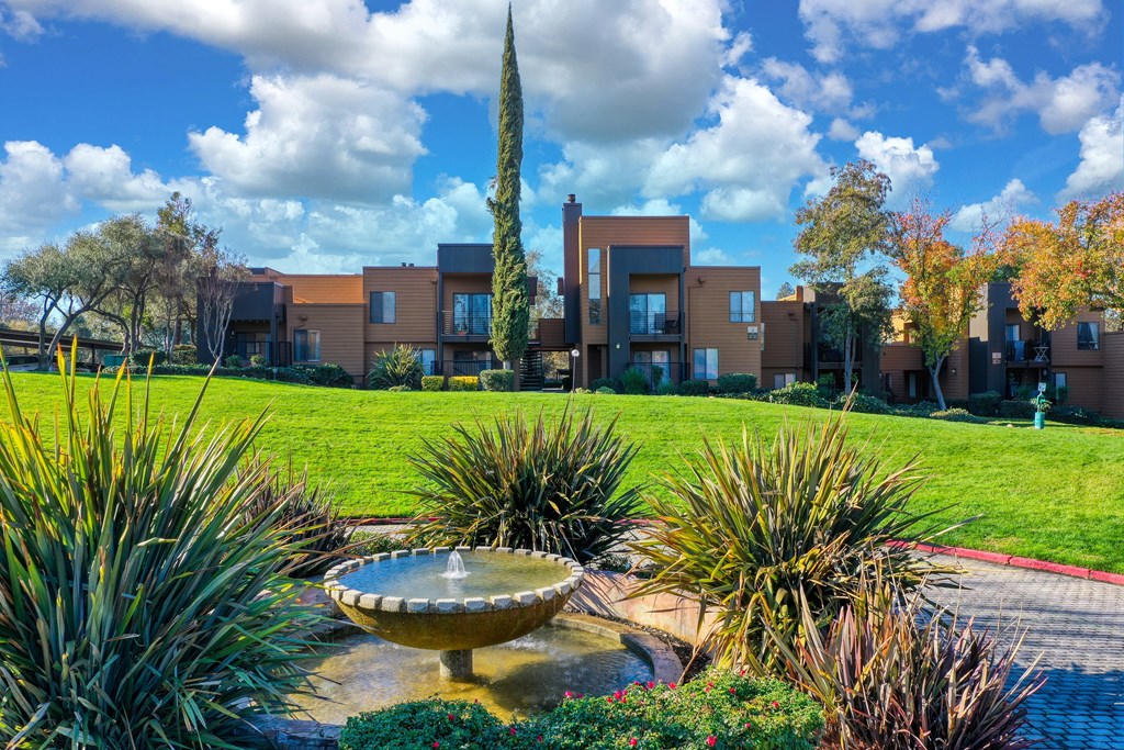 a fountain in the middle of a grassy area with apartment buildings in the background at Fountains of Fair Oaks, Fair Oaks
