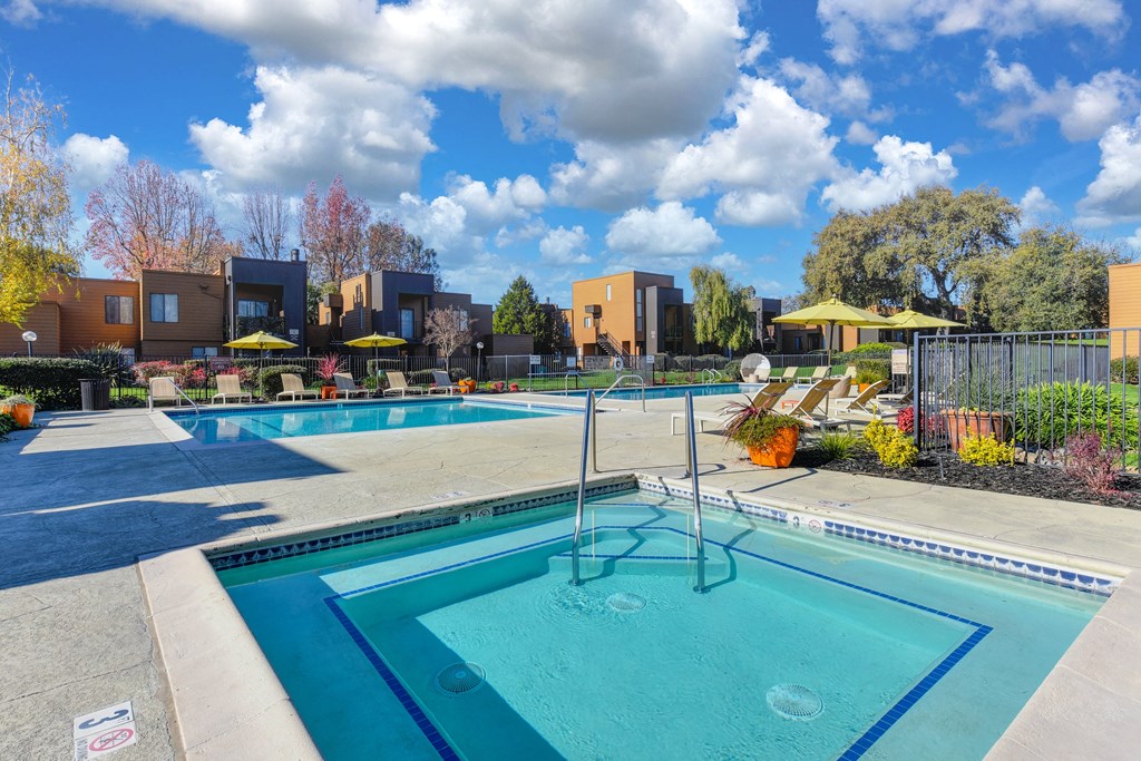 Community Spa with swimming pool and property buildings in the distance.  Blue skies and large white clouds in the sky.at Fountains of Fair Oaks, Fair Oaks, CA