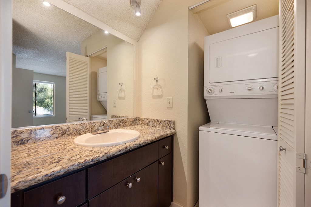 Bathroom with large mirror, granite vanity with sink and larger sized washer and dryer nearby at Fountains of Fair Oaks, California