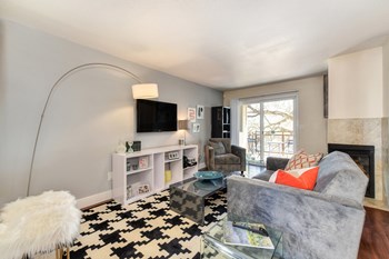 Model Living room with gray couch and chair. Sliding glass patio door leading to the balcony and fireplace in the corner. - Photo Gallery 3