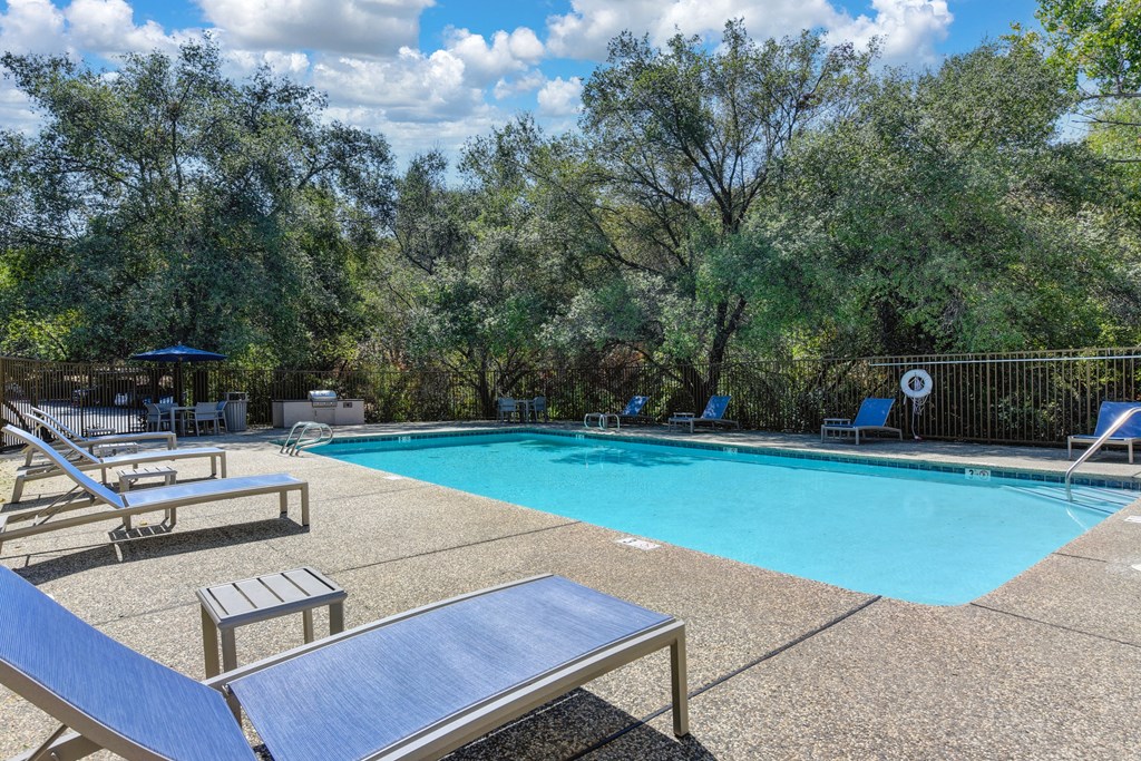 One of several swimming pools on-site.  This one is surrounded by oak trees in the distance.  Deck has lounge chairs and tables.at Folsom Ranch, Folsom, CA