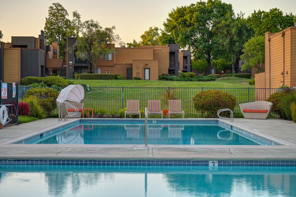 A pool surrounded by a fence and chairs.