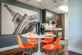 Model Dining area with table and 4 orange chairs. View of the kitchen area in the distance. Hardwood inspired flooring through out the dining and kitchen area. - Photo Gallery 5