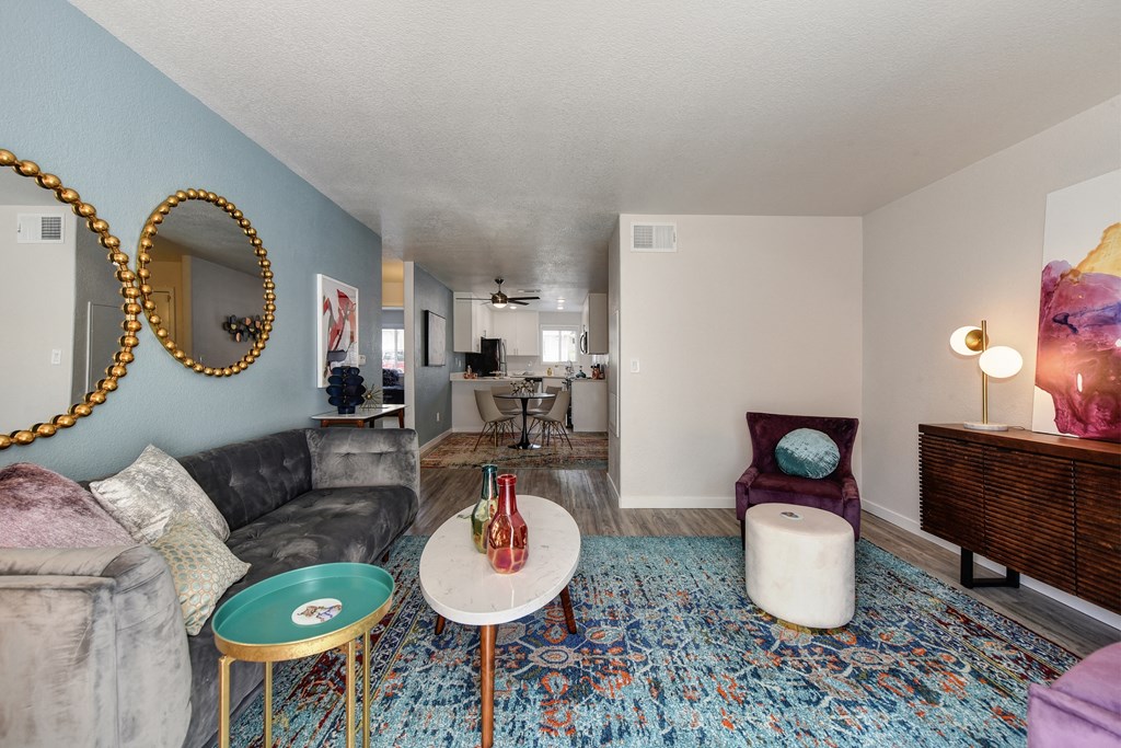 Living Room with Blue Pattern Rug, White Table, Gray Sofa, Purple Chair and Round Wall Mirrors at The Legacy Apartments, Antelope, CA