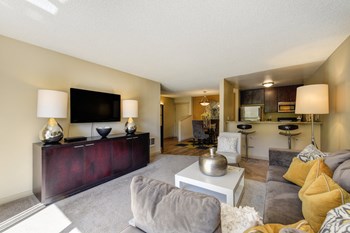 Model Living room with gray couch and white chair. Kitchen and counter with bar stools is visible from the living room. - Photo Gallery 5