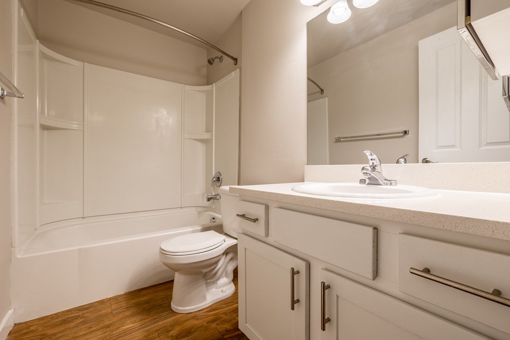 Vacant home bathroom with tub/shower enclosure, white sink/vanity with white cabinets and a white toilet