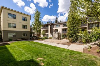 an outdoor area with grass and trees in front of an apartment building
