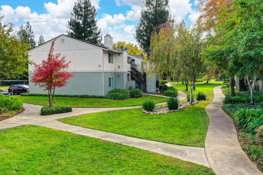 Community grounds with pedestrian walk paths surrounded by mature trees, green grass and shrubs at Monte Bello Apartments, California, 95826