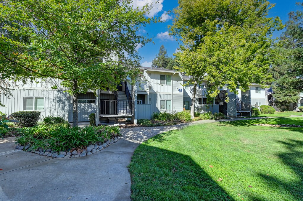 Monte Bello Community grounds with mature tress and landscaping around the building.  Concrete walk path  at Monte Bello Apartments, Sacramento
