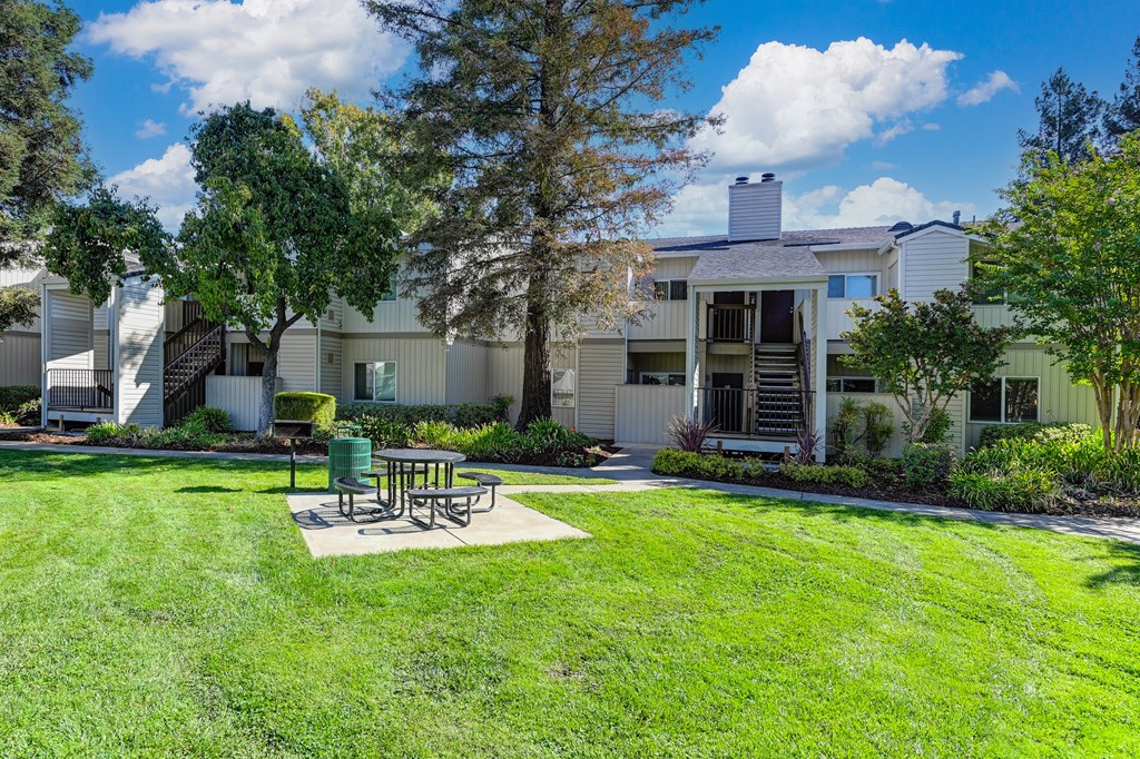One of a few community picnic areas that have table, BBQ and trashcan.  This one is in the middle of a grassy area with apartment buildings in the distance. at Monte Bello Apartments, Sacramento, Cali