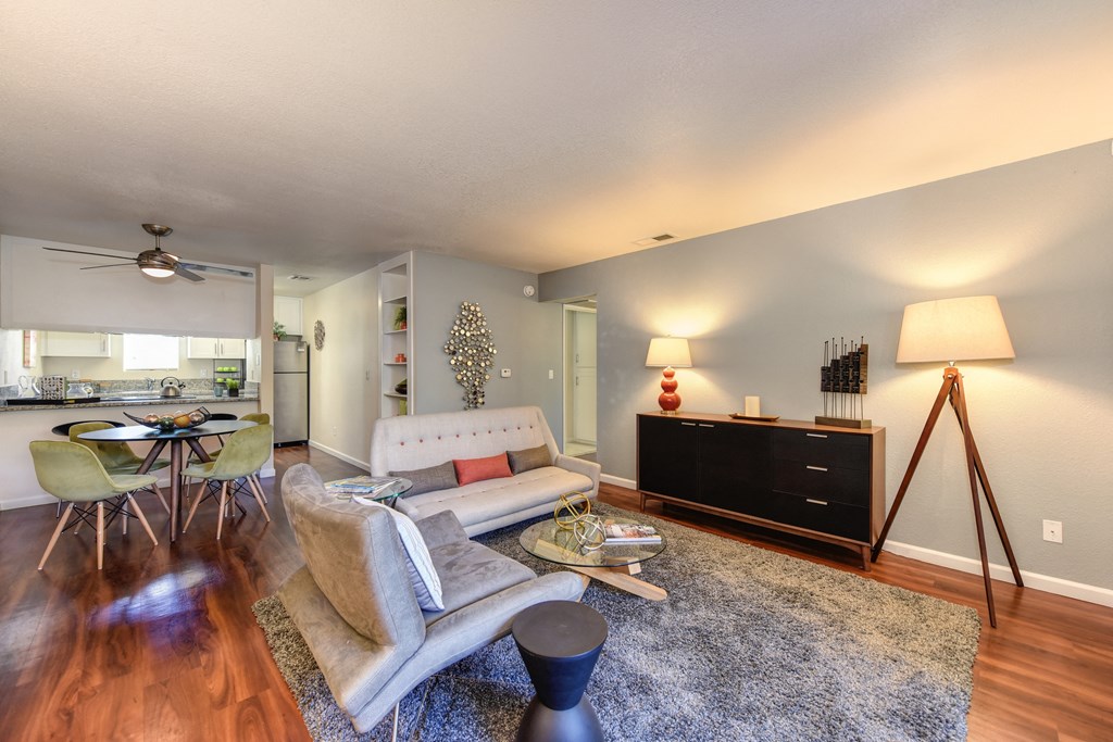 Living Room with light colored accent wall, Hardwood Inspired Floors, Gray Rug, Lamps, and White Sofa at Monte Bello Apartments, Sacramento, CA