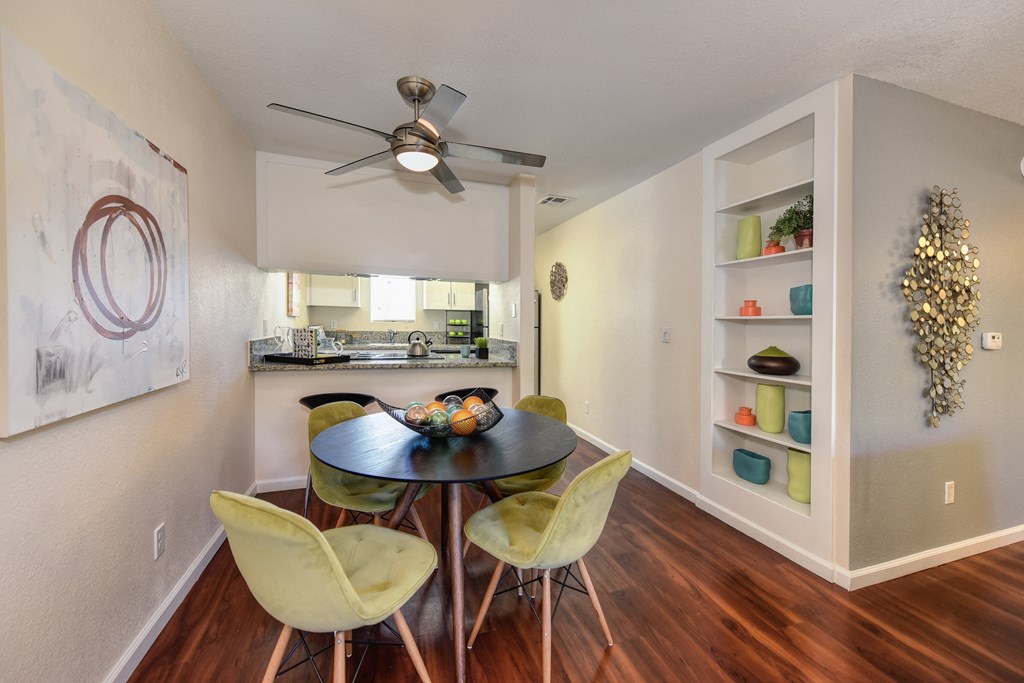 Dining Area with View of Kitchen, Built In Storage, Hardwood Inspired Floors, Yellow Chairs, Black Round Table and Ceiling Fan/Light at Monte Bello Apartments, California