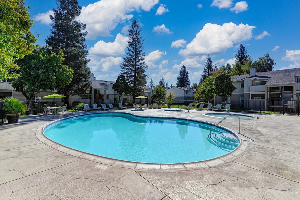 Monte Bello Swimming pool area with spa and apartment buildings in the distance.  Mature trees and blue skies in the background. at Monte Bello Apartments, Sacramento, California