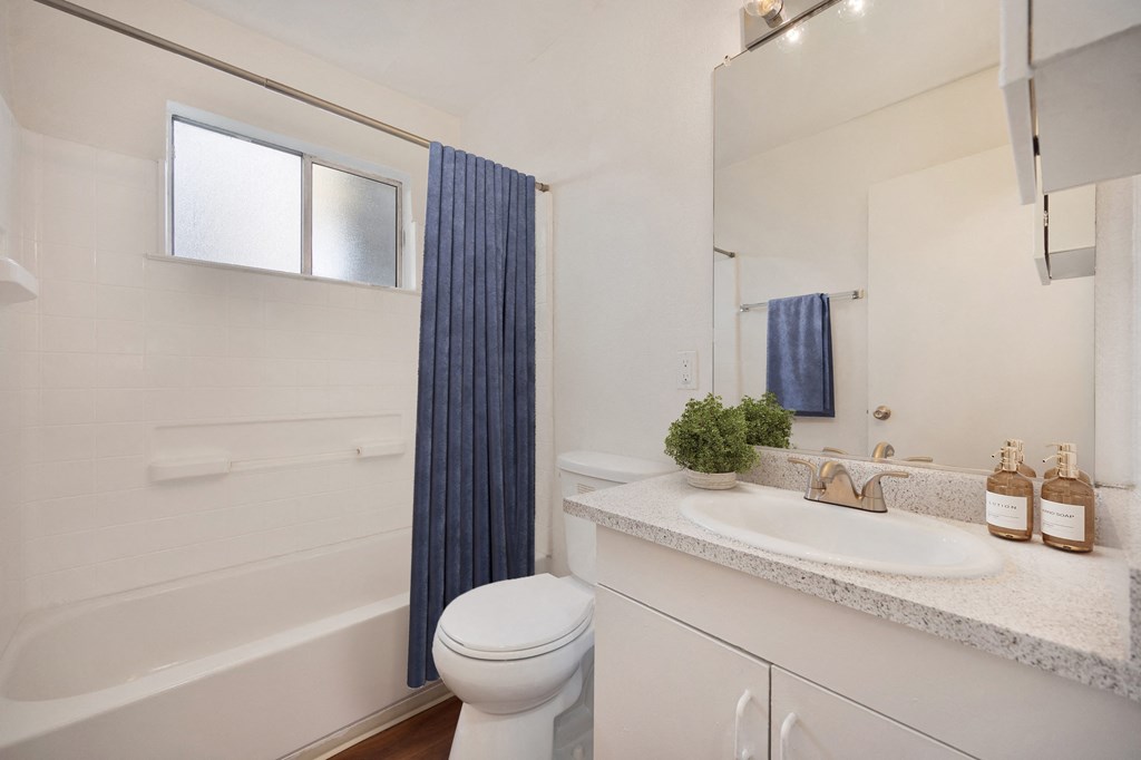 A white bathroom with a white toilet and a white sink. at Olympus Park Apartments, California