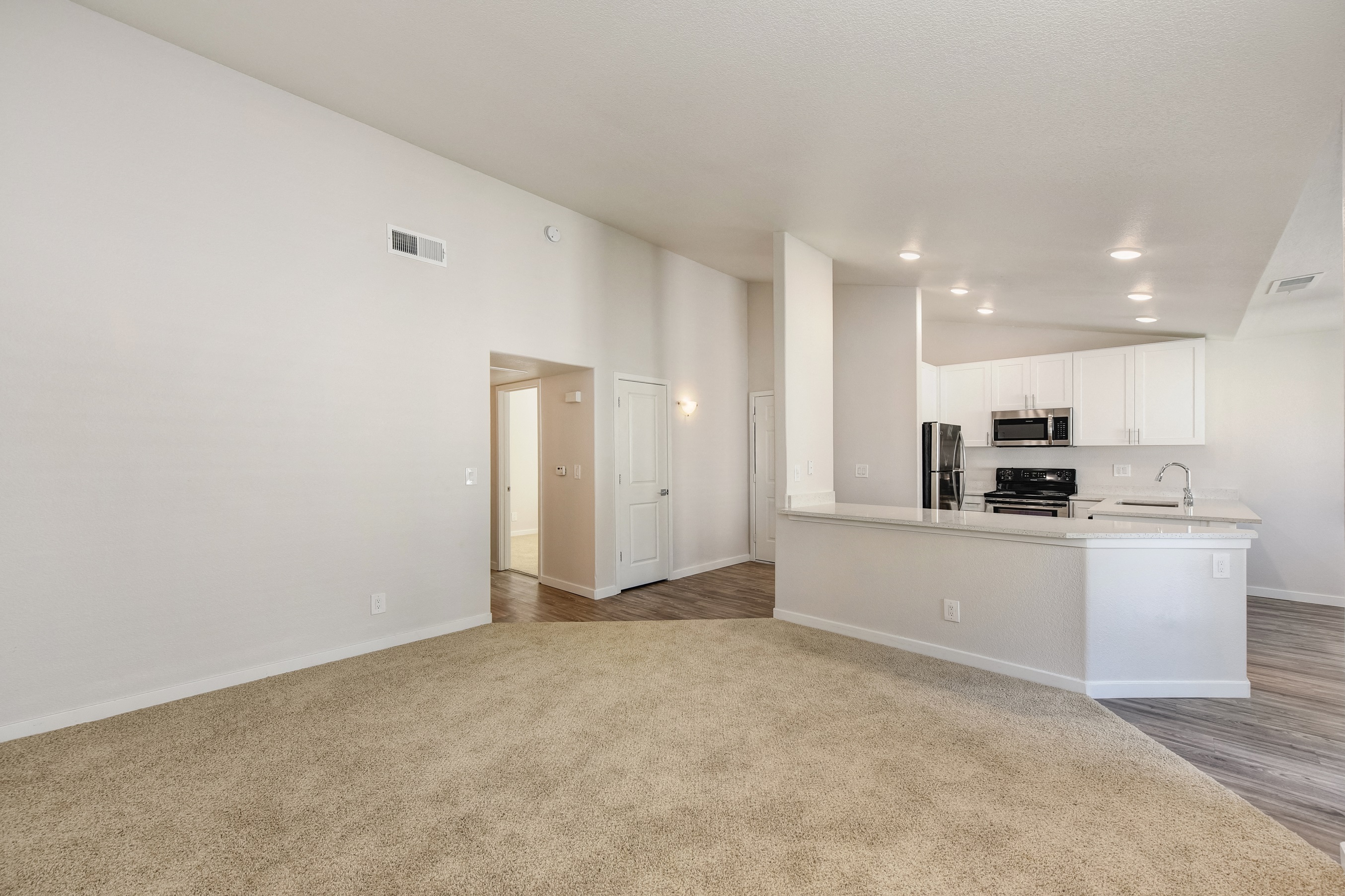 Living Room with View of Kitchen, Carpet, White Counter and Hardwood Inspired Floor by Door at The Legacy Apartments, Antelope, California