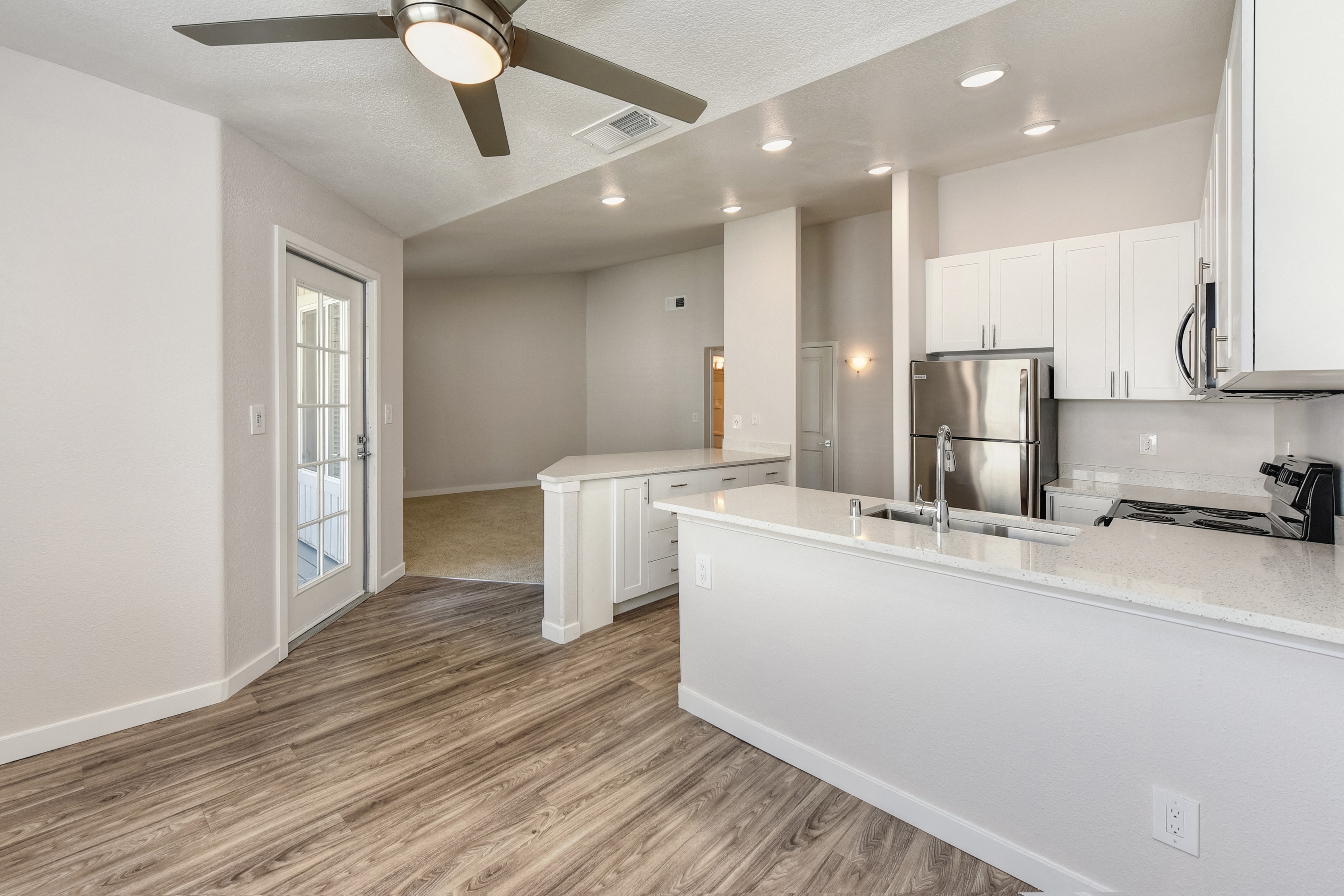 Open Kitchen with Wood Inspired Floors, Ceiling Fan/Light, White Counter and Refrigerator at The Legacy Apartments, California