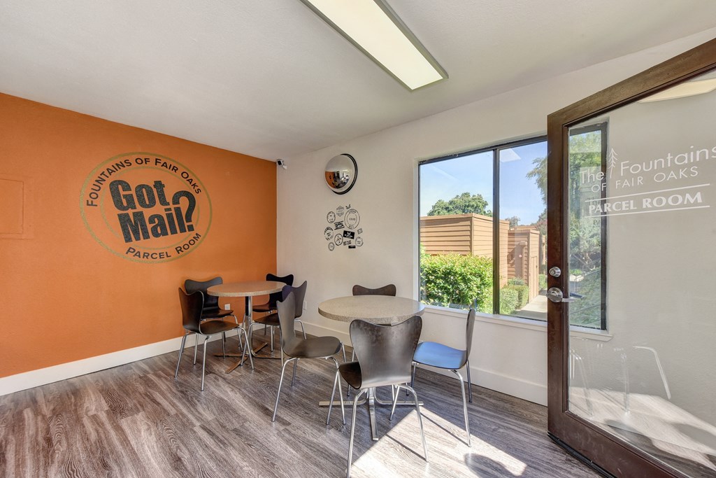 Parcel Room with Hardwood Inspired Floor, Short Round Tables, Chairs, Orange Wall with at Fountains of Fair Oaks, Fair Oaks