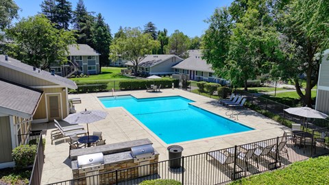 a swimming pool with lounge chairs and umbrellas in front of a house at Pinecrest Apartments, Davis ,95616