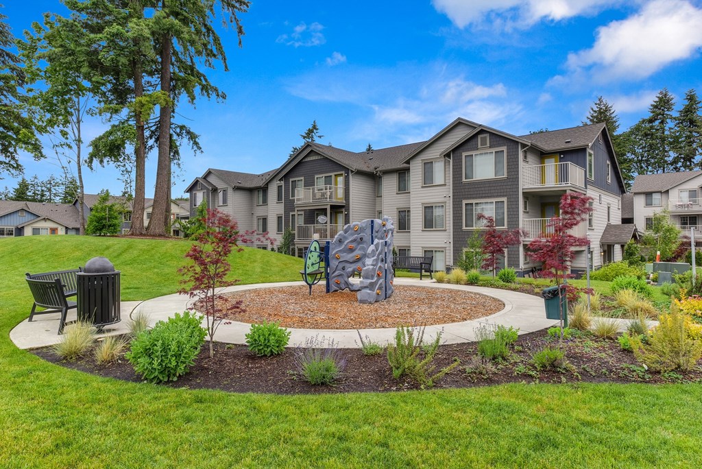 Outdoor Play Area with Mini Rock Climbing Aparatus, Wood Chip Floor, Grass, Bench, and Apartment Exteriors