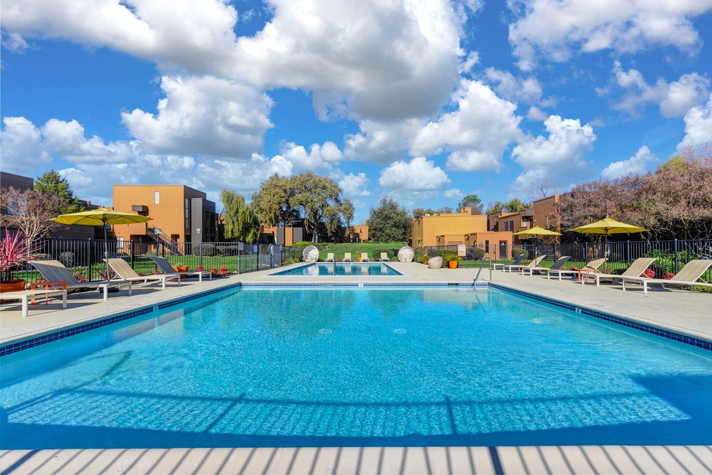 Swimming pool on-site with yellow umbrellas, tables and chairs around to pool deck.  Colorful flowers and landscaping surrounding the pool area.at Fountains of Fair Oaks, Fair Oaks, 95628