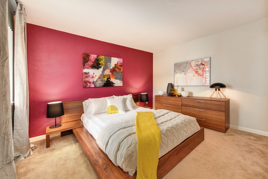Red Wall Bedroom with Full Sized Mattress and Wooden Frame, White Comforter and Yellow Blanket, Wood Dresser, Abstract Painting at Addison Ranch Apartments, Petaluma, CA