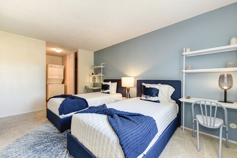 Model home bedroom with two beds and a desk with a chair. Stackable washer and dryer inside room at Renaissance Park Apartments, Davis, California